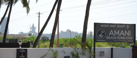 A sign for Amani Beach Home Stay with a view of palm trees and a statue in the background.