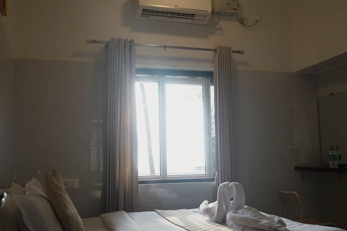 A hotel room with a bed, a window with curtains, an air conditioning unit, and a small table with bottles.