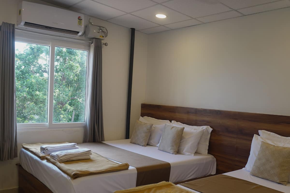 A hotel room with two beds, a window with curtains, an air conditioning unit, and a ceiling fan.