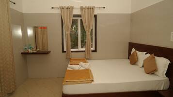 A hotel room with a bed, a window with curtains, a small shelf with toiletries, and a mirror.