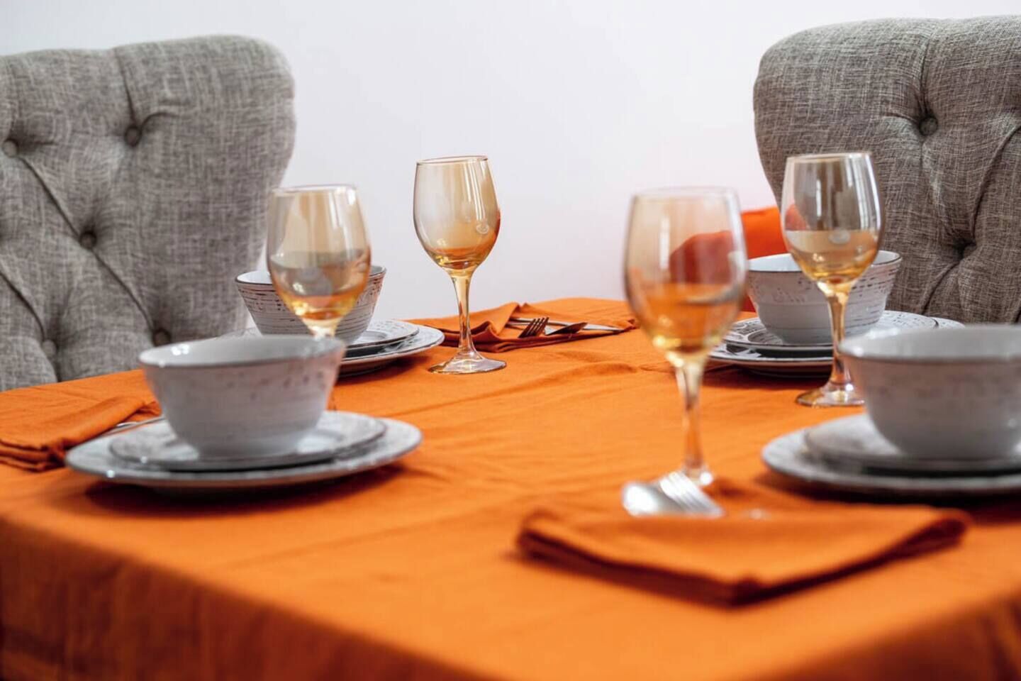 A dining table set with white bowls and wine glasses, surrounded by grey upholstered chairs.