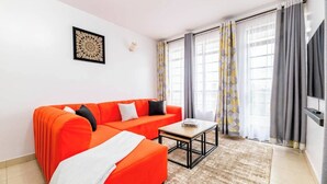 Ein modernes Wohnzimmer mit einem leuchtend orangefarbenen Sofa, einem kleinen Couchtisch und einem flachbildfernseher an der Wand.