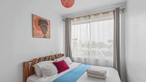 Un dormitori amb un llit, una finestra amb cortines i una obra d'art penjada a la paret.