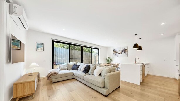 A modern living room with a sectional sofa, a wooden side table, and a kitchen area with a sink and countertop. - Fishermen (Torquay)