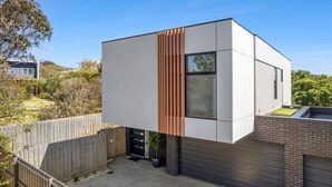 A modern two-story house with a flat roof, a wooden slatted wall, and a brick base. - Fishermen (Torquay)