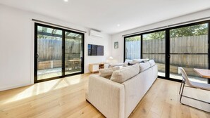 A spacious living room with a large sofa, a dining table, and sliding glass doors leading to a backyard. - Fishermen (Torquay)