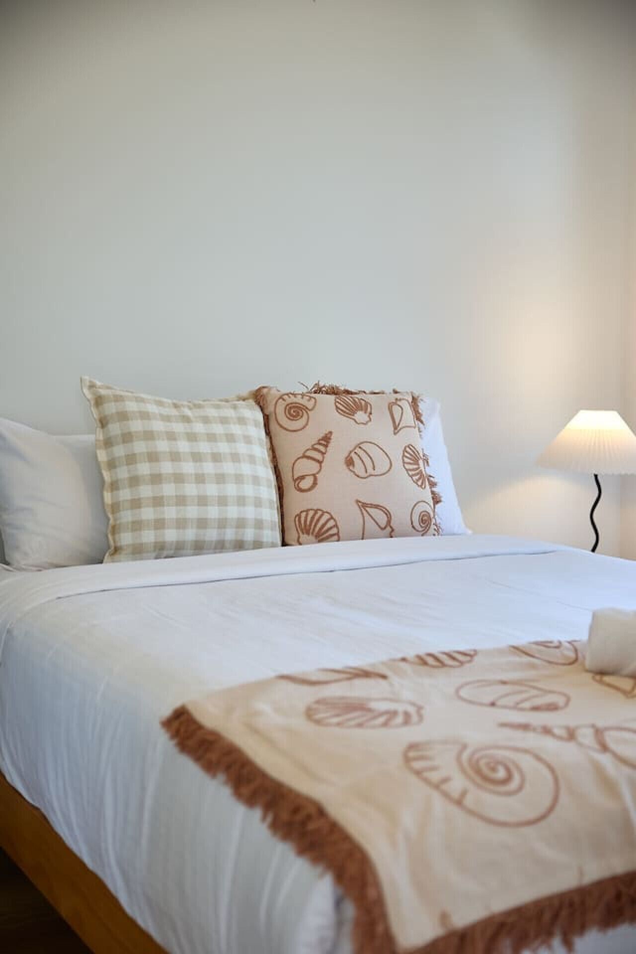 A neatly made bed with white bedding and a beige blanket with a scalloped edge.