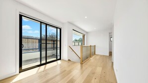 A spacious room with a large sliding glass door leading to an outdoor area, a wooden staircase, and a view of the sky. - Fishermen (Torquay)