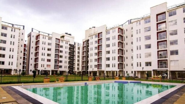 A modern apartment complex with a central swimming pool, multiple balconies, and a well-maintained lawn area.