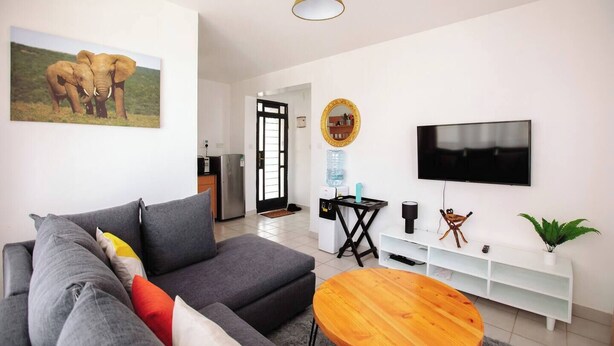 Ein modernes Wohnzimmer mit einem grauen Sofa, einem Holztisch, einem Fernseher und einem Elefantenbild.