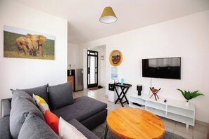 Una sala de estar moderna con un sofá gris, una mesa de centro de madera, un televisor y un cuadro de elefantes.