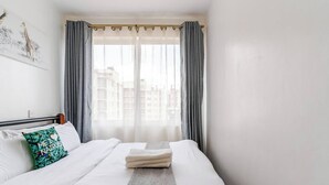 Ein Hotelzimmer mit Bett, einem Fenster mit Vorhängen, Blick auf die Stadt und einer Wand mit einem Giraffenbild.