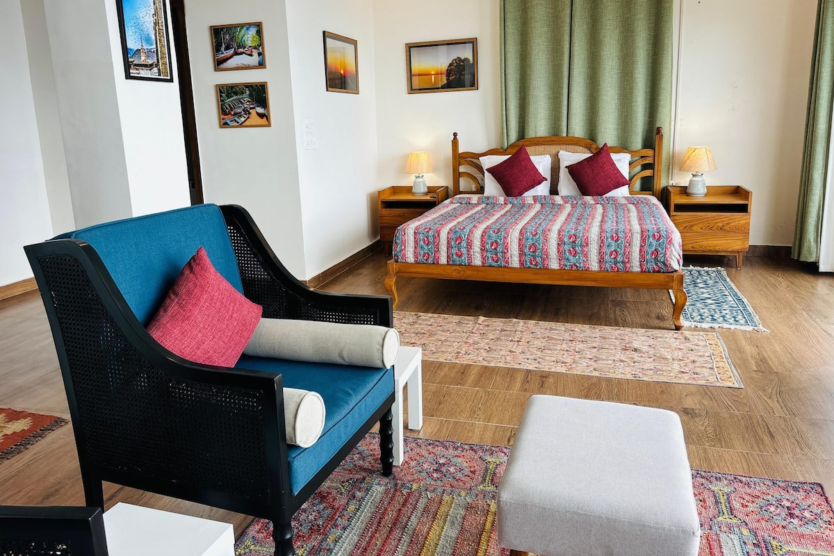 A bedroom with a bed, a chair, a nightstand, a lamp, and a wall with pictures.