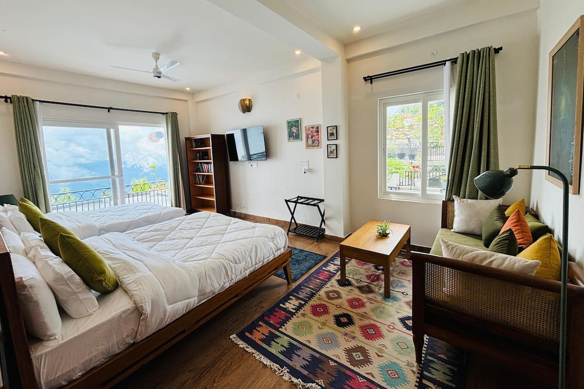 A bedroom with a large bed, a small table, a sofa, a TV, and a balcony with a view.