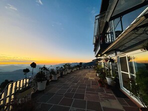 Une terrasse agrémentée de plantes en pot, un sentier en pierre et une vue sur les montagnes lointaines au coucher du soleil.