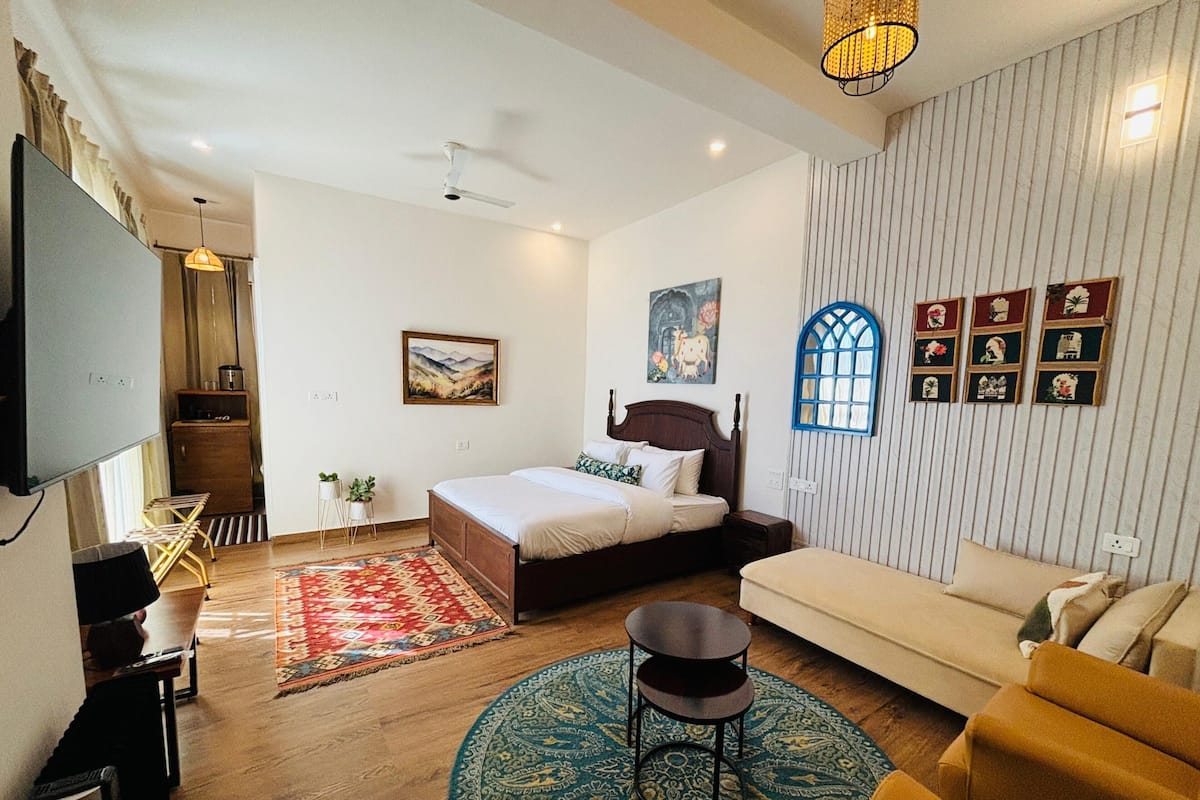 A bedroom with a bed, a sofa, a TV, and a small table.