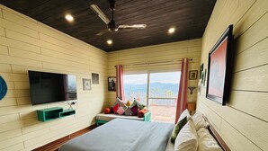A bedroom with a bed, a TV, a ceiling fan, and a view of the outdoors.