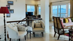 A spacious living area with a high ceiling, a staircase, and a balcony with mountain views.