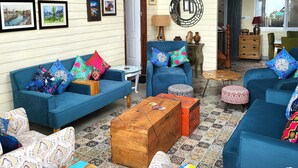 A spacious living area with blue sofas and colorful cushions, a wooden coffee table, and a large mirror on the wall.