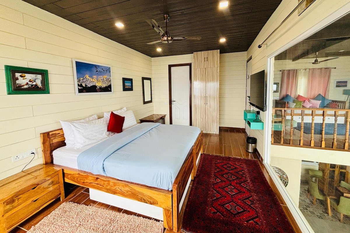 A bedroom with a wooden bed, a red rug, and a balcony with a view.