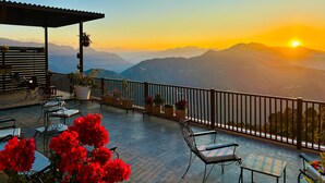 A terrace with outdoor seating, potted plants, and a view of distant mountains during sunset. - The Ridge House - A Villa Community (Tehri)