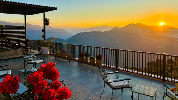 A terrace with outdoor seating, potted plants, and a view of distant mountains during sunset.