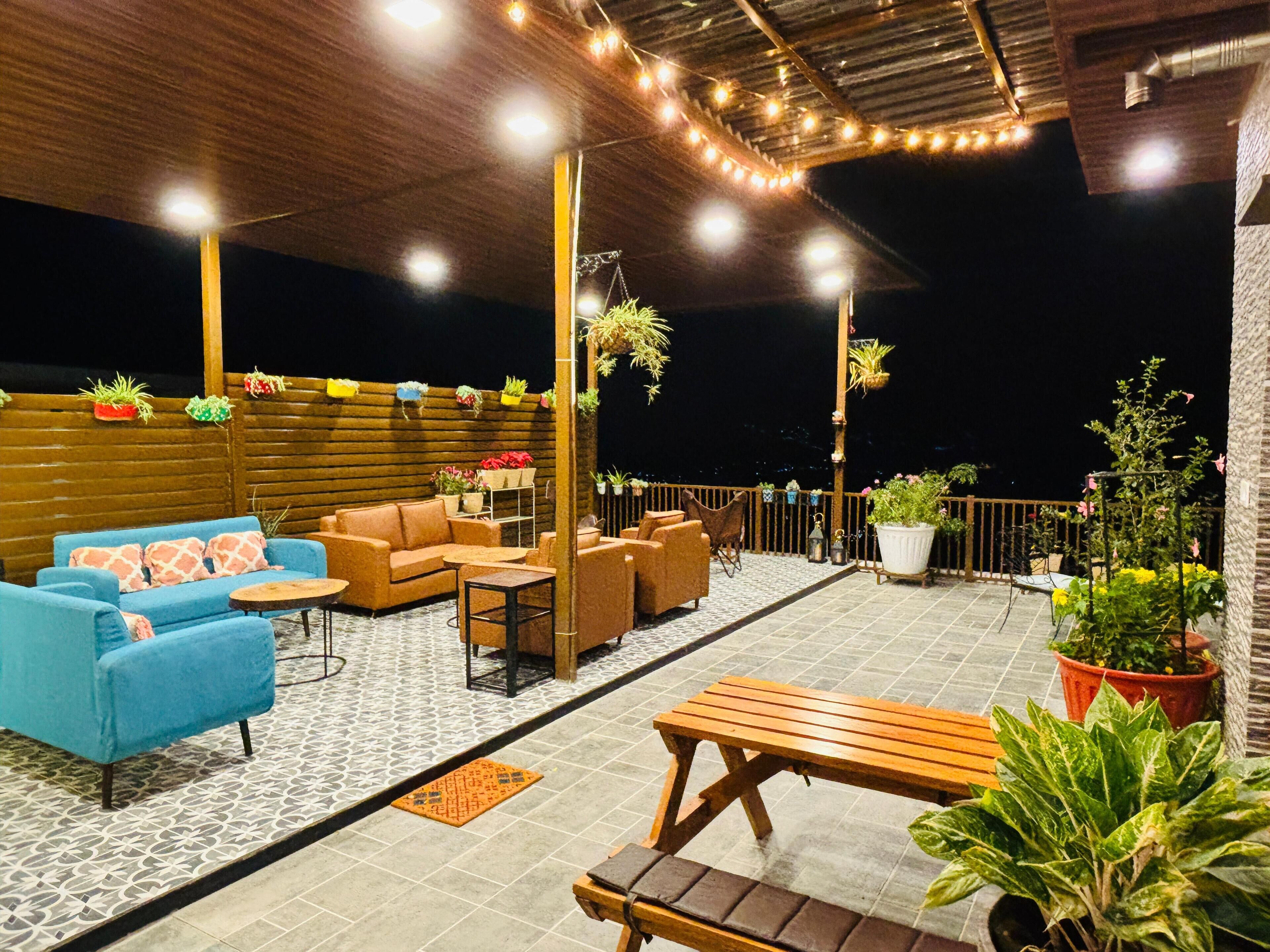 Un patio al aire libre con arreglos de asientos, plantas en macetas y luces colgantes.