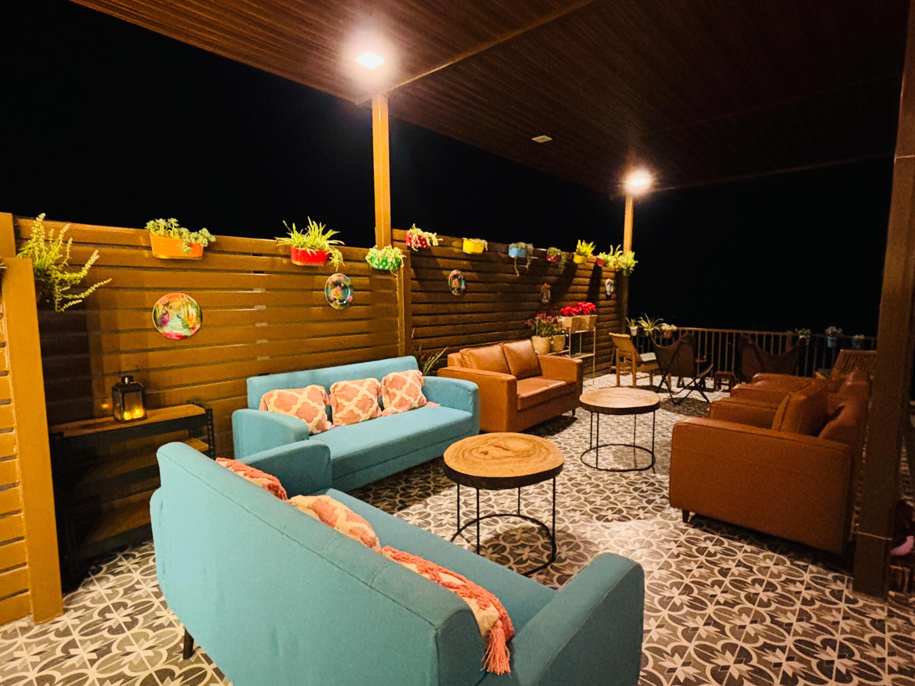 An outdoor seating area with sofas and chairs, a patterned floor, and a wooden wall with potted plants.