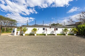 Un edificio con camino de grava, paredes blancas y varias plantas en macetas.