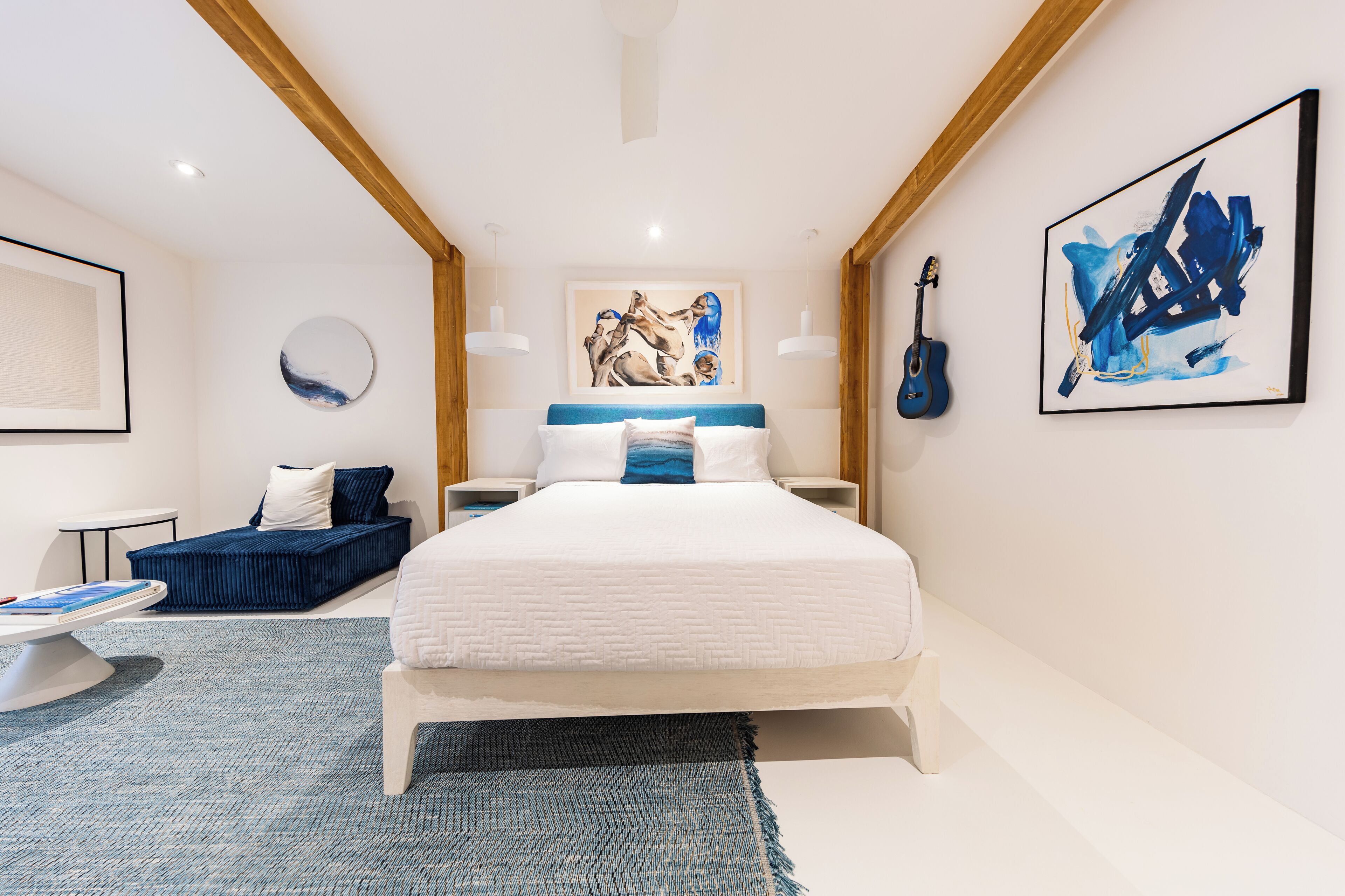 A modern bedroom with a large bed, a blue sofa, a round mirror, and artwork on the walls.