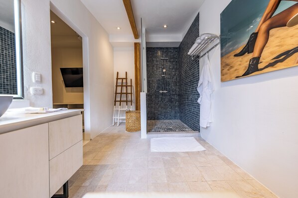 A modern bathroom with a shower, a sink, and a large mirror. - Wanderust Suites (San Juan del Sur)