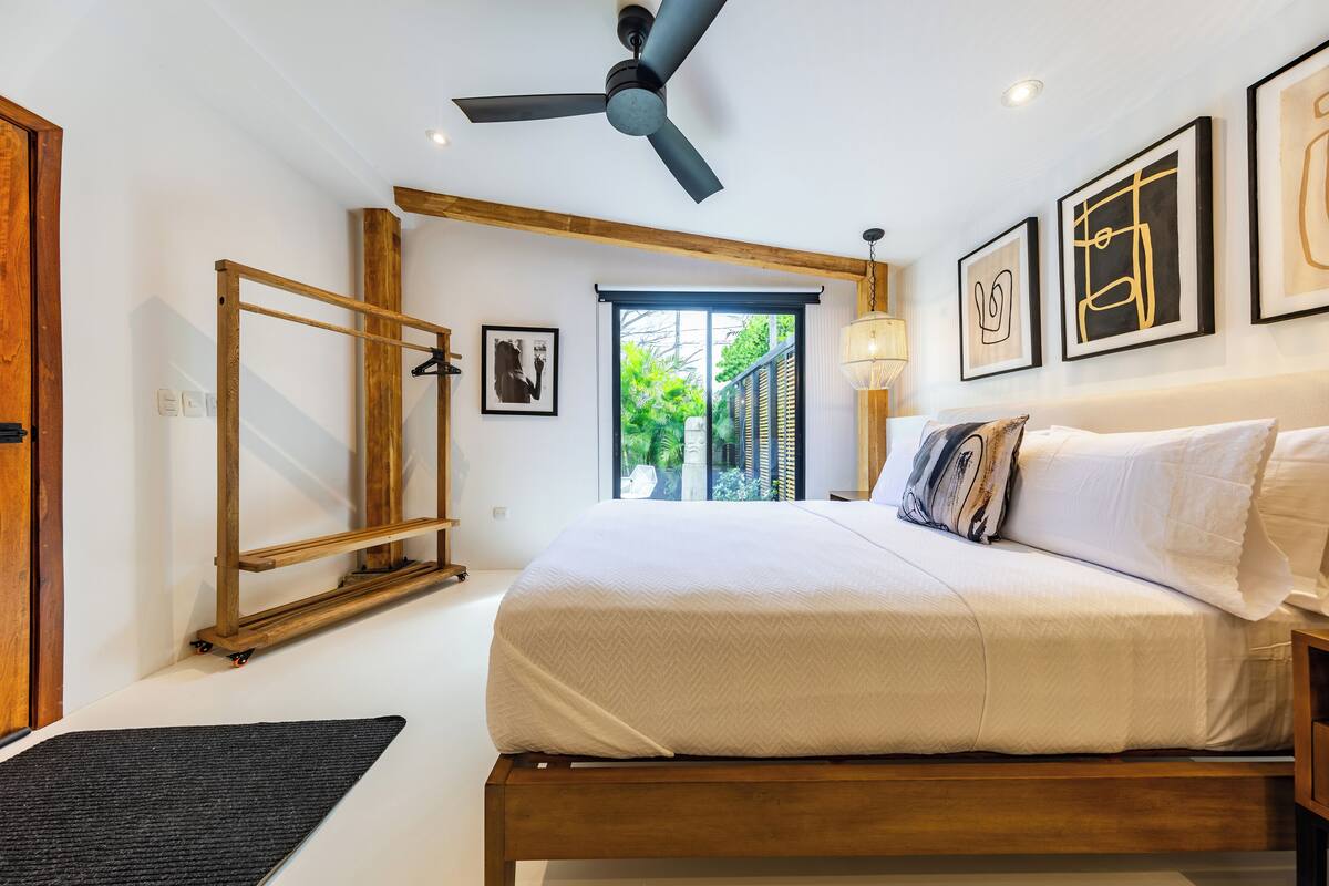 Un dormitorio con cama, ventilador de techo, obras de arte y vistas al exterior.