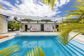 Una piscina con cubierta blanca, dos sofás blancos con cojines rosados y vista al cielo.