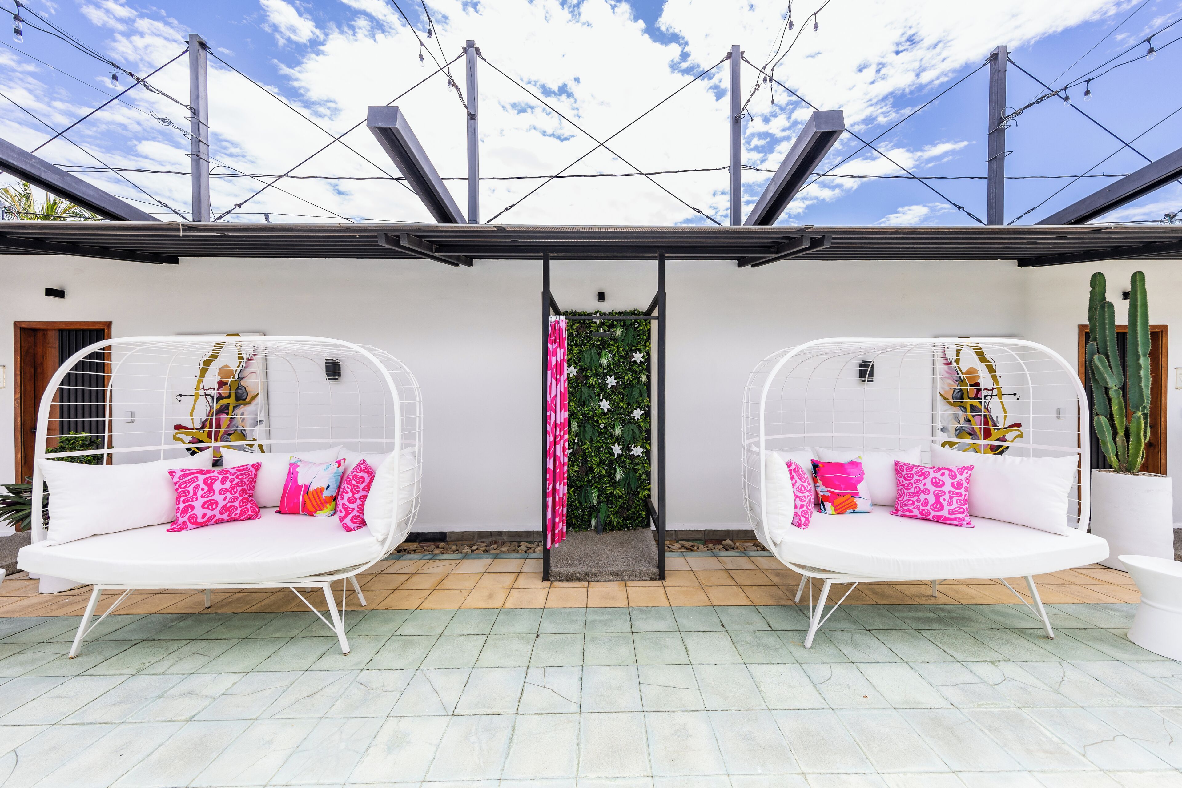 A modern outdoor seating area with two white cushioned chairs, each with a metal frame and pink patterned cushions.