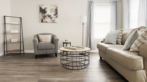 A living room with a round coffee table, a sofa, a patterned armchair, and a bookshelf. - Riverside A3 -EVV 1BR-1BA Apt (Evansville)