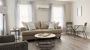 A living room with a beige sofa, a round coffee table, patterned chairs, and a dining table with chairs. - Riverside A3 -EVV 1BR-1BA Apt (Evansville)
