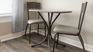 A dining area with a table and two chairs, a window with a curtain, and a framed picture on the wall. - Riverside A3 -EVV 1BR-1BA Apt (Evansville)