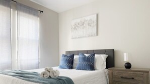 A neatly arranged bedroom with a bed, pillows, a bedside table, and a wall-mounted artwork. - Riverside A3 -EVV 1BR-1BA Apt (Evansville)