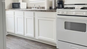 A kitchen with white cabinets, a microwave, a coffee maker, and a stove. - Riverside A3 -EVV 1BR-1BA Apt (Evansville)