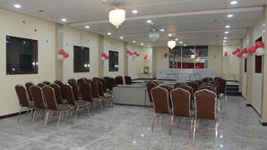 A conference room with rows of chairs, a stage, and a chandelier. - Hotel Subhadra (Kannauj)