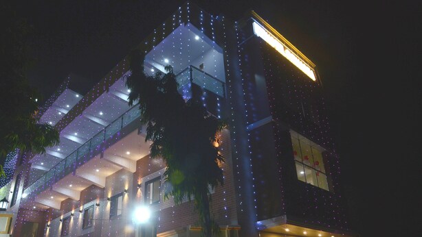 A multi-story building with balconies and a glass facade at night, illuminated by string lights. - Hotel Subhadra (Kannauj)