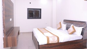 A bedroom with a wooden bed, a nightstand, and a wall-mounted TV. - Hotel Subhadra (Kannauj)