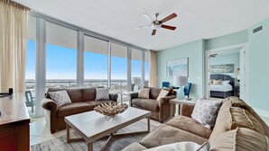 A spacious living room with a large window, a ceiling fan, and a view of the city.