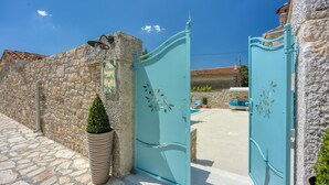 A stone wall with a turquoise gate, a potted plant, and a clear blue sky. - Lovely home in Selina (Selina)
