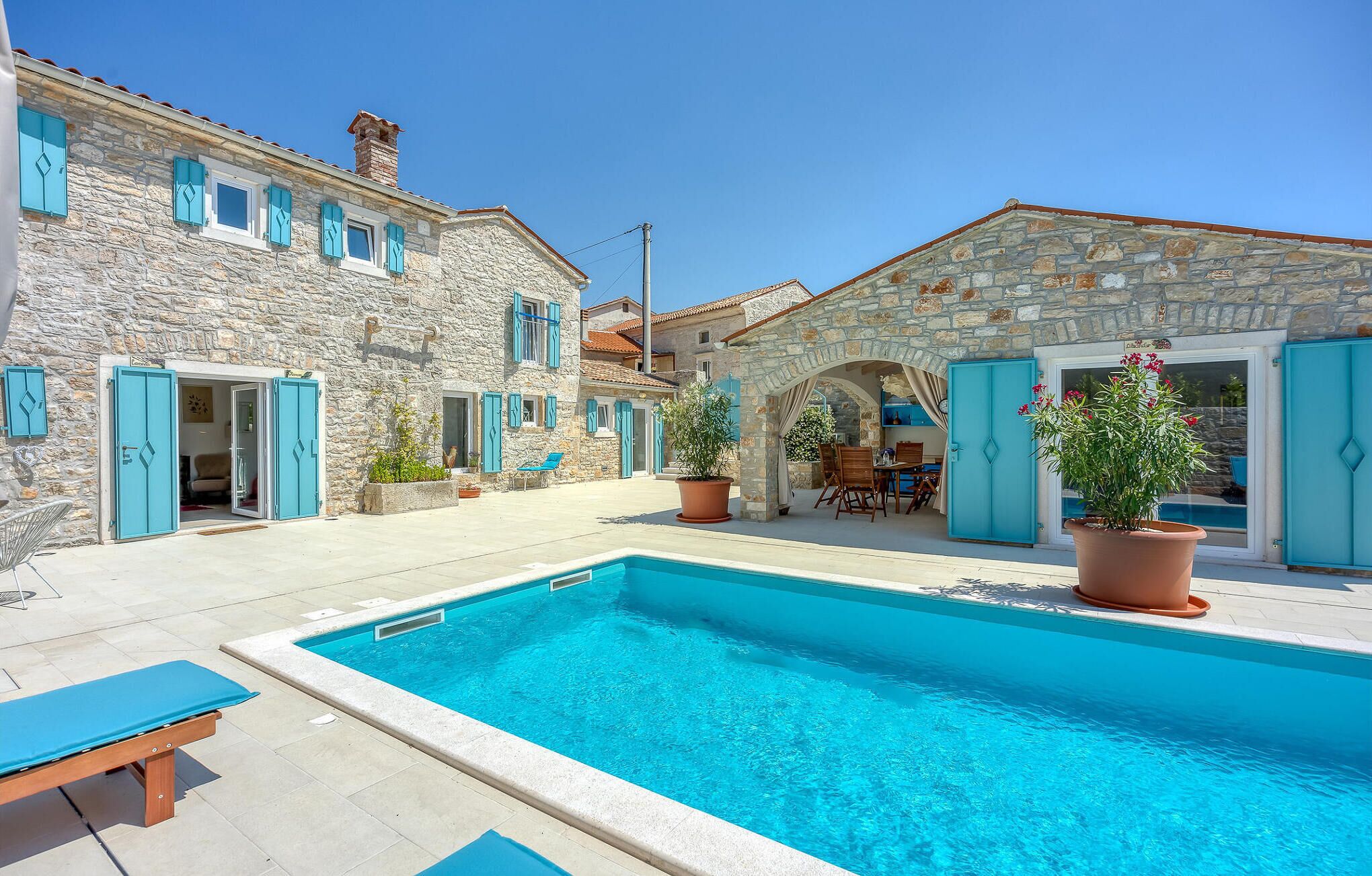 A stone building with a swimming pool, outdoor seating, and potted plants.
