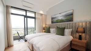 A large bed with white bedding, two bedside tables with lamps, a view of the city through a large window, and a painting on the wall.