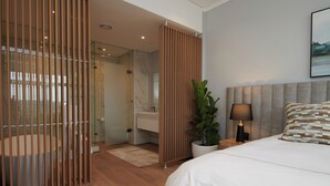 A modern bedroom with a large bed, a bedside table with a lamp, a potted plant, and a view of a bathroom with a glass shower enclosure.