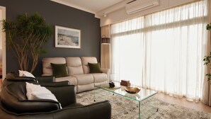A modern living room with a beige sofa, a glass coffee table, and a large window with sheer curtains.