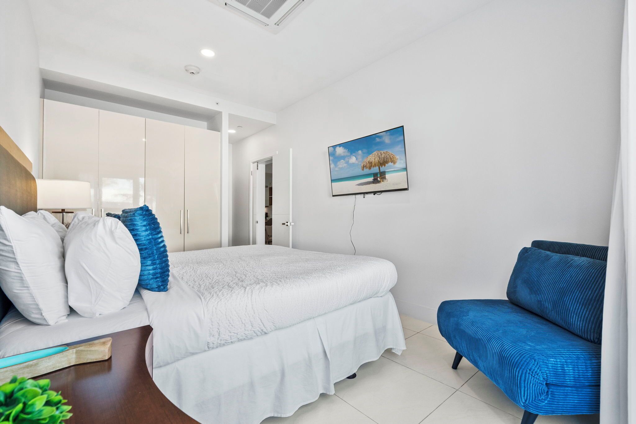 Ein Schlafzimmer mit einem Bett, einem blauen Sofa, einem Bild mit Strandmotiv und einem Kleiderschrank.