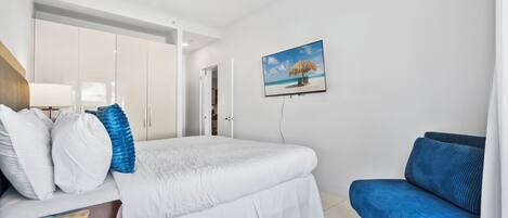 Ein Schlafzimmer mit einem Bett, einem blauen Sofa, einem Bild mit Strandmotiv und einem Kleiderschrank.